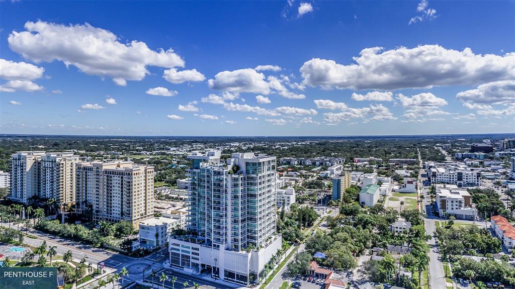 An aerial view shows a modern high-rise apartment building surrounded by urban development and trees — 555 QUAY COMMONS UNIT 2001, SARASOTA, FL