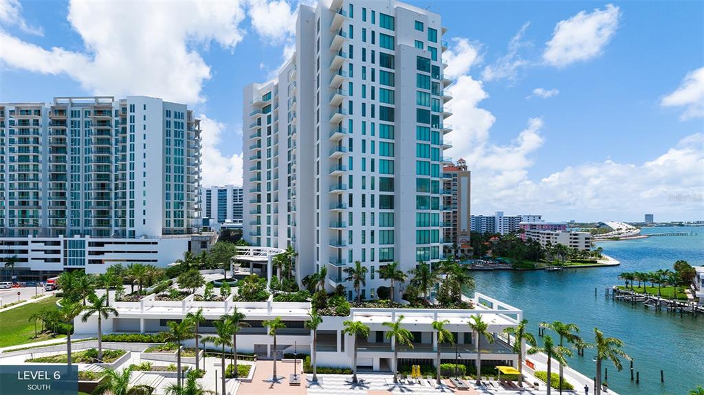 An exterior view shows a tall white residential building with balconies overlooking a waterfront area — 555 QUAY COMMONS UNIT 2001, SARASOTA, FL