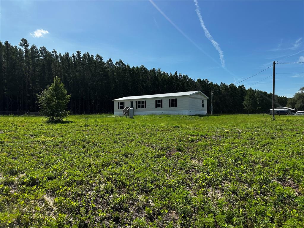 A single-story manufactured home sits on a large, grassy lot bordered by a dense forest — 7351 NE 106TH TERRACE, BRONSON, FL