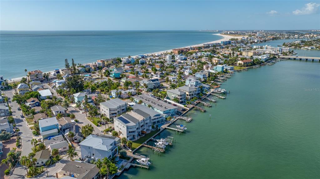 An aerial view shows a coastal neighborhood with houses situated between the ocean and bay — 8575 SUNSET COURT, TREASURE ISLAND, FL