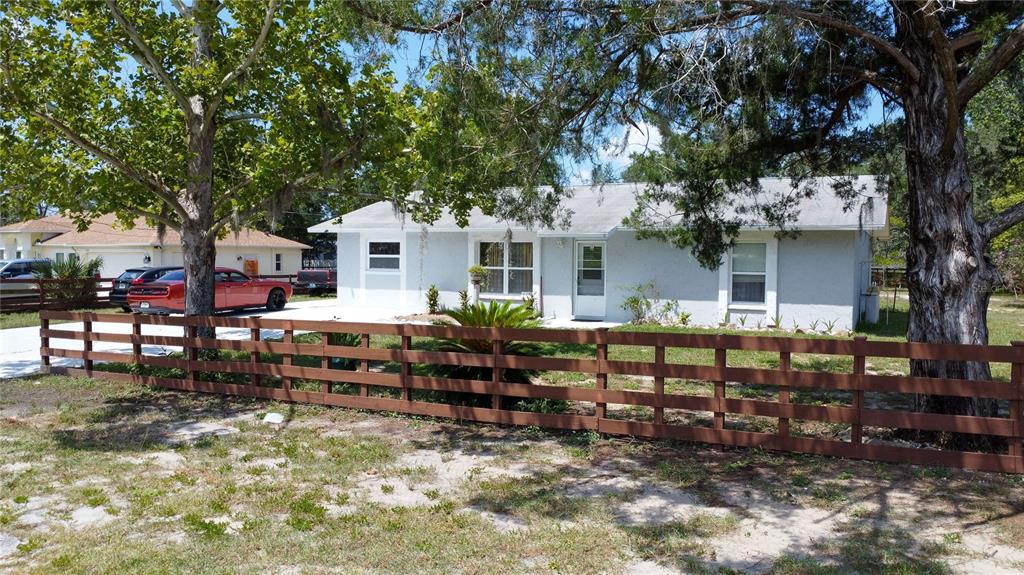 A single-story house with a light-colored exterior sits behind a brown wooden fence — 8301 WEEPING WILLOW STREET, BROOKSVILLE, FL