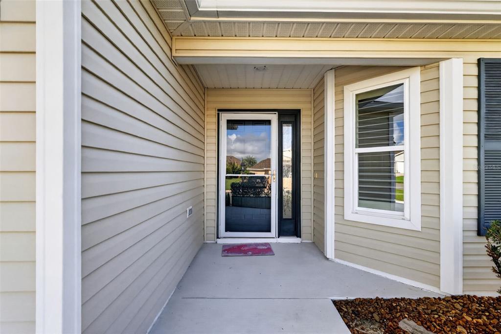 A covered entryway features light-colored horizontal siding, a glass storm door, and a concrete porch — 3305 FINK STREET, THE VILLAGES, FL