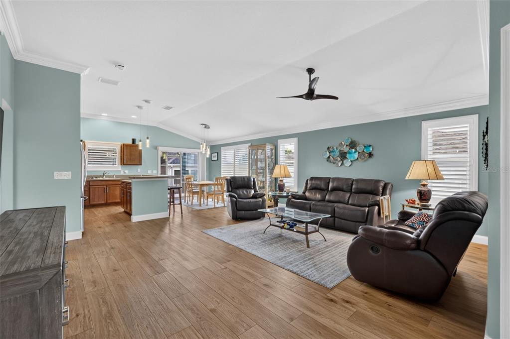 An open-concept living room and kitchen with light blue walls and wood-look tile flooring — 3305 FINK STREET, THE VILLAGES, FL