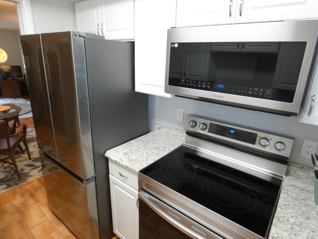 A kitchen features stainless steel appliances, white cabinets, and speckled granite countertops — 1701 PINEHURST ROAD UNIT 9G, DUNEDIN, FL