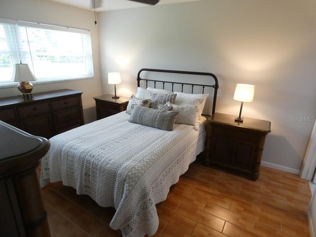 A bedroom features a metal bed frame, wooden nightstands, a dresser, and tile flooring — 1701 PINEHURST ROAD UNIT 9G, DUNEDIN, FL