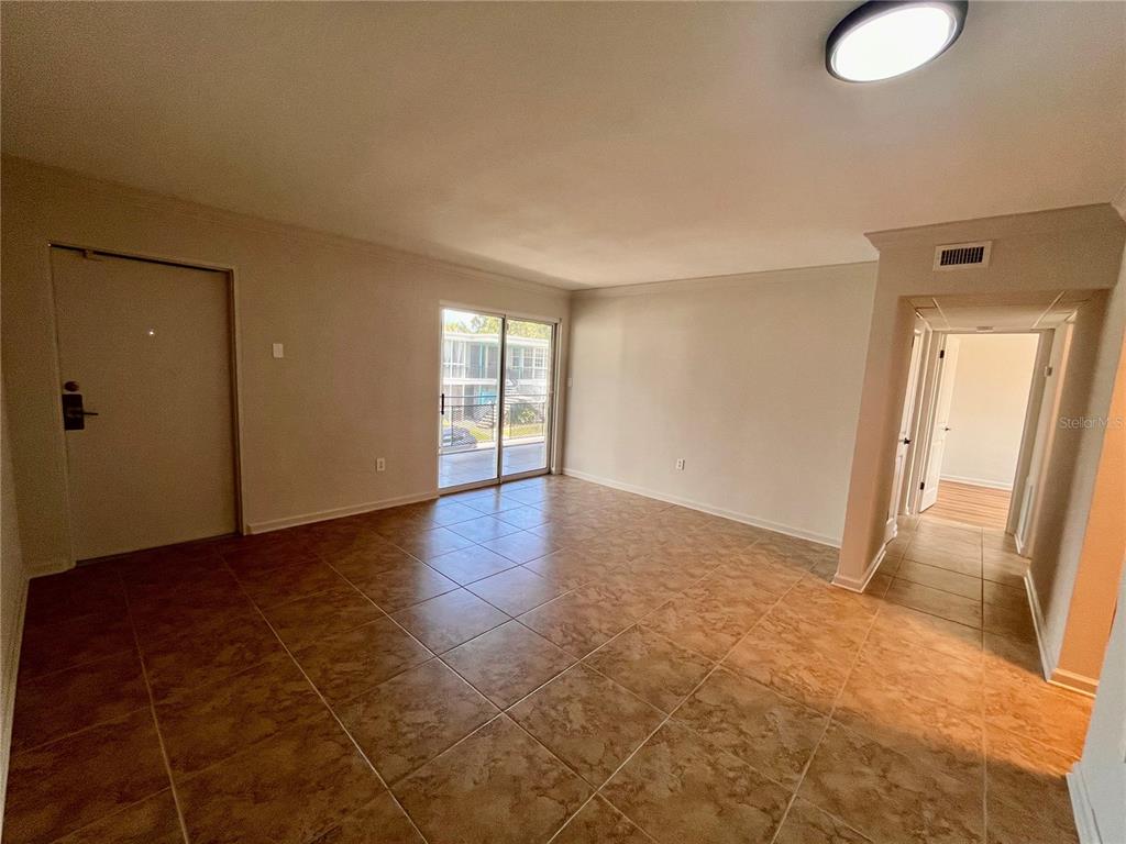 An empty living room features beige tile flooring, a sliding glass door, and a hallway entrance — 151 N ORLANDO AVENUE UNIT 242, WINTER PARK, FL