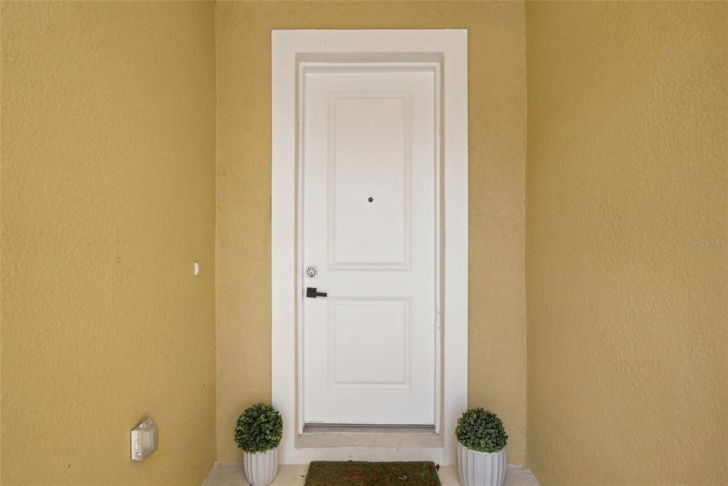 A white front door is centered on a tan stucco wall with two potted plants — 11957 SKY ACRES TERRACE, LAKEWOOD RANCH, FL
