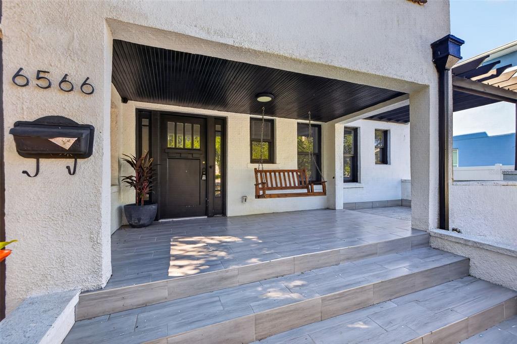 A two-story white stucco house features a front porch, a pergola, and a grassy yard — 6566 1ST AVENUE S, ST PETERSBURG, FL