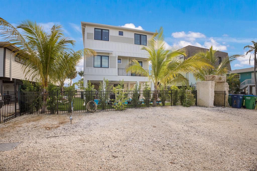 A three-story white house with a gravel driveway, fenced yard, and palm trees — 2415 AVENUE B, BRADENTON BEACH, FL