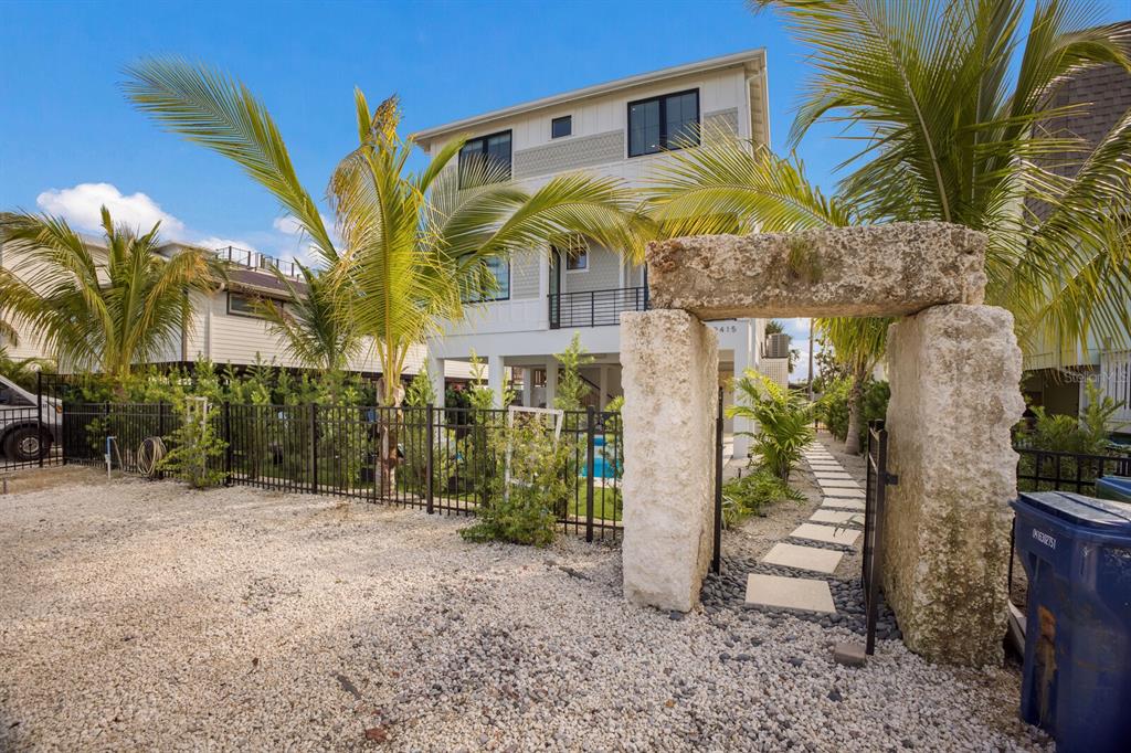 A three-story house with a stone archway entrance, palm trees, and a gravel driveway — 2415 AVENUE B, BRADENTON BEACH, FL