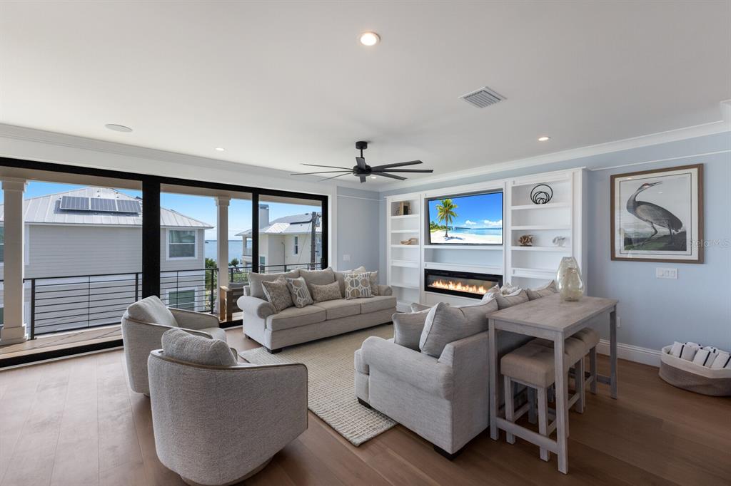 A living room features a fireplace, built-in shelving, a sofa, armchairs, and a balcony view — 2415 AVENUE B, BRADENTON BEACH, FL