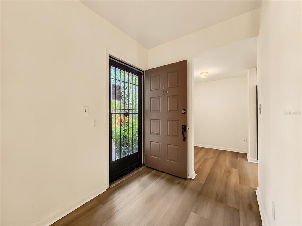 An entryway features wood-look flooring, a brown front door, and a black storm door — 1701 COURTYARD WAY UNIT 105, NAPLES, FL