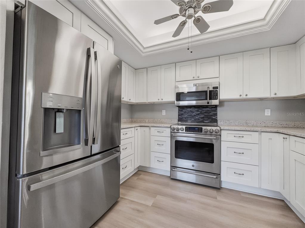 A kitchen with white cabinets, stainless steel appliances, speckled countertops, and light wood-look flooring — 1701 COURTYARD WAY UNIT 105, NAPLES, FL