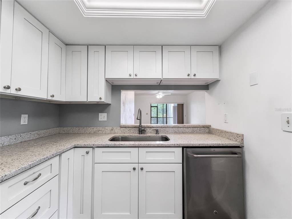 A kitchen features white shaker cabinets, granite countertops, a stainless steel sink, and a dishwasher — 1701 COURTYARD WAY UNIT 105, NAPLES, FL