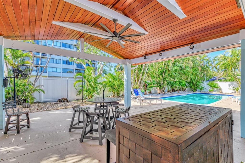 A covered patio features a wood-paneled ceiling, a ceiling fan, dining furniture, and a pool — 5628 CAPE LEYTE DRIVE, SARASOTA, FL