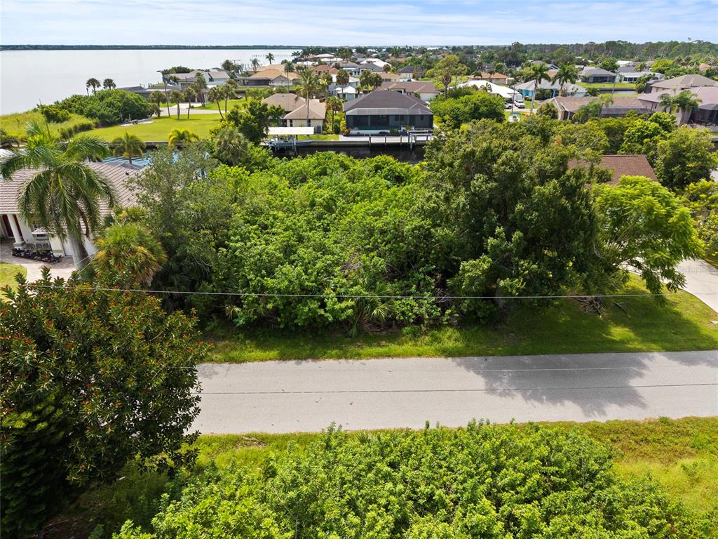 An aerial view shows a vacant, tree-covered lot situated between houses near a waterfront canal — 2434 HERRON TERRACE, PORT CHARLOTTE, FL