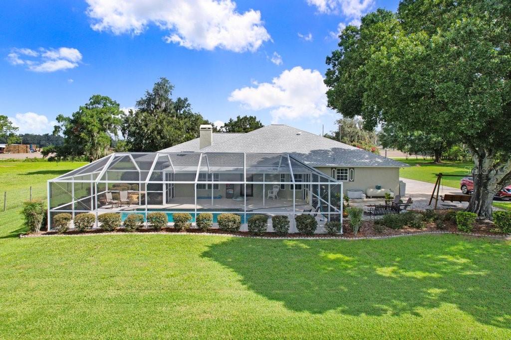 A rear view of a house with a screened-in pool and a large grassy yard — 13221 TOM GALLAGHER ROAD, DOVER, FL