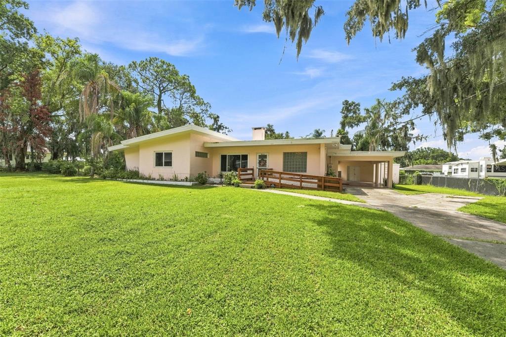 A single-story peach-colored house with a wooden wheelchair ramp and a carport on a lawn — 1311 E TOMLIN STREET, PLANT CITY, FL