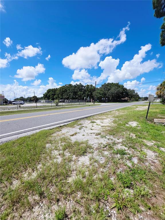 A grassy lot sits beside a paved road with trees and buildings in the background — 305 E BRIDGERS AVENUE, AUBURNDALE, FL