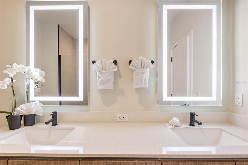 A double vanity bathroom features two illuminated mirrors, white countertops, and matte black fixtures — 17244 BLESSING DRIVE, CLERMONT, FL