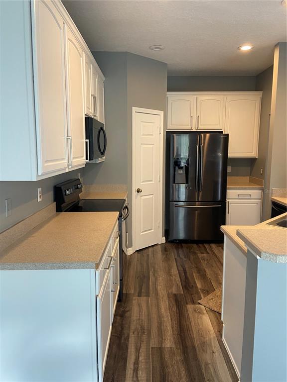 A kitchen features white cabinets, stainless steel appliances, tan countertops, and wood-look flooring — 27546 PLEASURE RIDE LOOP, WESLEY CHAPEL, FL
