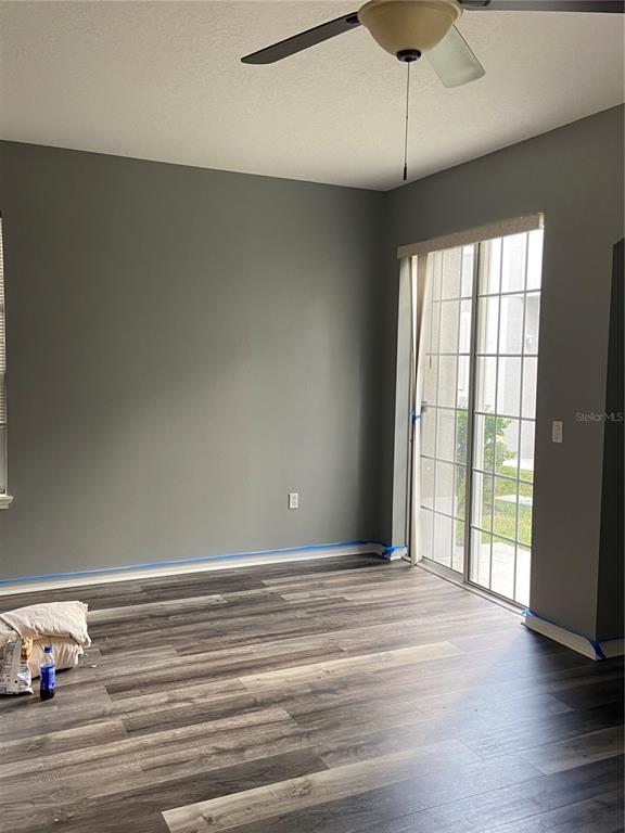 An empty room features gray walls, wood-look flooring, a ceiling fan, and sliding glass doors — 27546 PLEASURE RIDE LOOP, WESLEY CHAPEL, FL