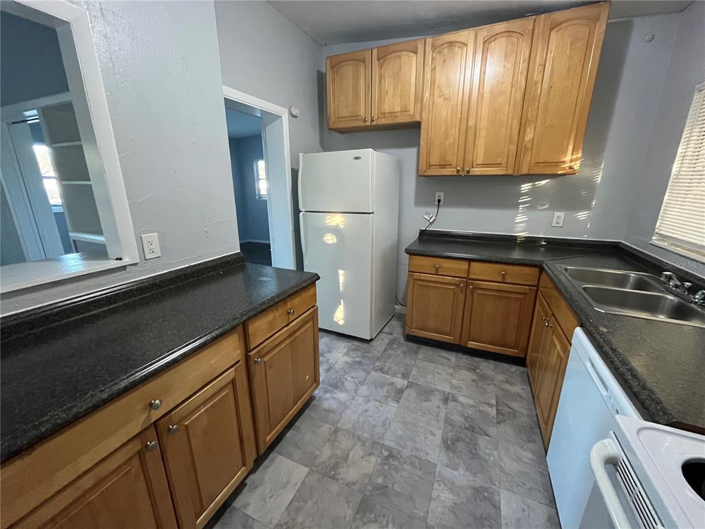 A kitchen features light wood cabinets, dark countertops, a white refrigerator, and gray flooring — 510 MANOR DRIVE, BARTOW, FL