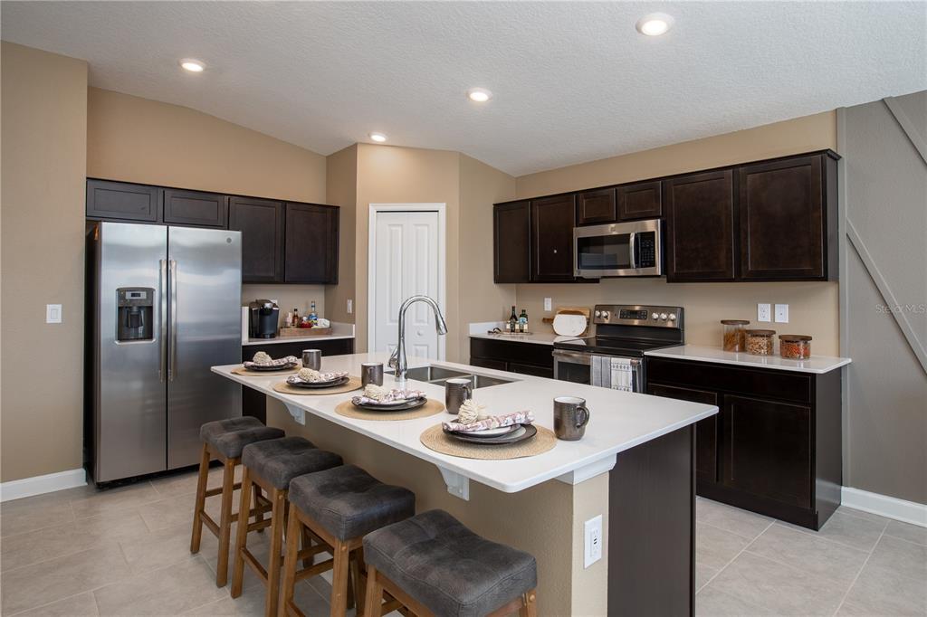 A kitchen features dark wood cabinets, stainless steel appliances, a white island, and bar stools — 5162 WORCHESTER DRIVE, KISSIMMEE, FL