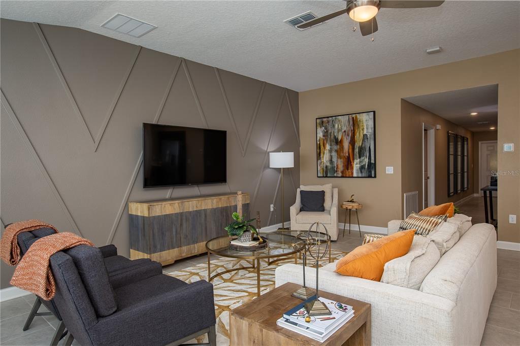 A living room features a geometric accent wall, a television, and neutral-toned furniture — 5162 WORCHESTER DRIVE, KISSIMMEE, FL