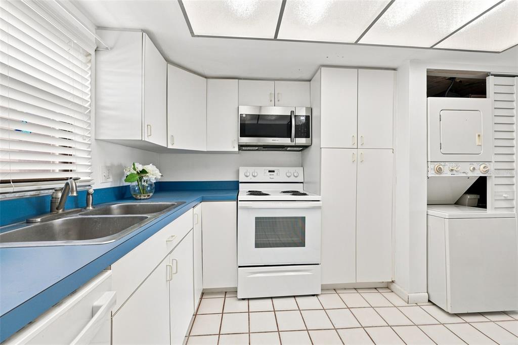 A kitchen features white cabinets, blue countertops, white appliances, and a stacked washer and dryer — 7050 SUNSET DRIVE S UNIT 610, SOUTH PASADENA, FL