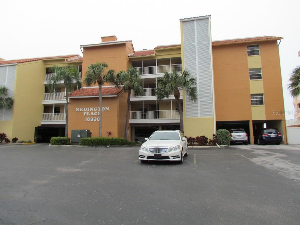 A multi-story apartment building with a parking area and palm trees in front — 16330 GULF BOULEVARD UNIT 304, REDINGTON BEACH, FL