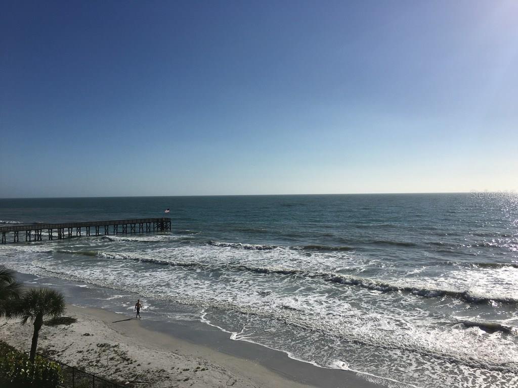 An elevated view of a sandy beach, ocean waves, and a wooden pier under clear skies — 16330 GULF BOULEVARD UNIT 304, REDINGTON BEACH, FL