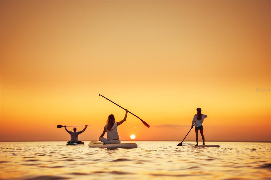 Three people paddleboard on the water during a vibrant orange sunset — 4502 BAHAMA DRIVE, HERNANDO BEACH, FL