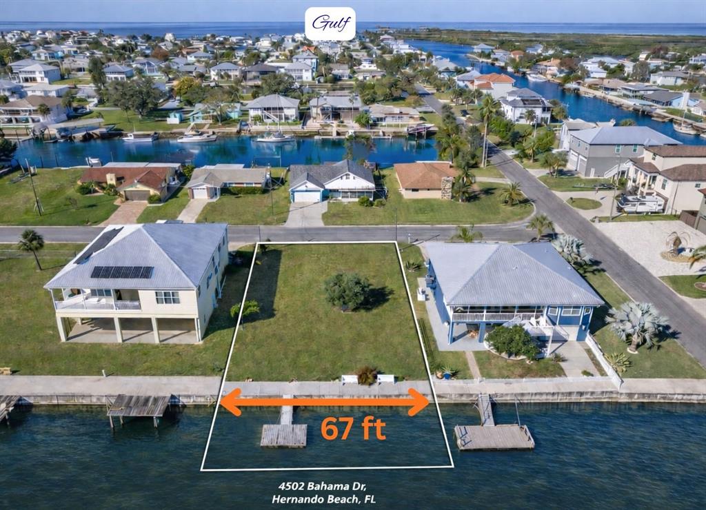 An aerial view shows a vacant waterfront lot with a dock between two elevated houses — 4502 BAHAMA DRIVE, HERNANDO BEACH, FL