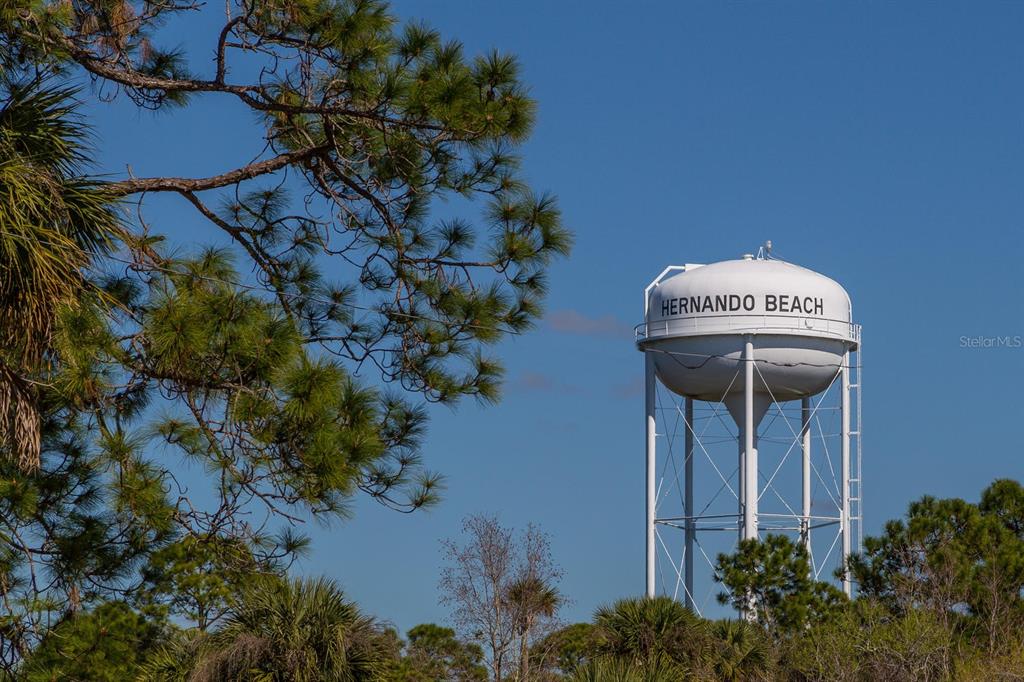 A white water tower labeled Hernando Beach stands against a clear blue sky — 4502 BAHAMA DRIVE, HERNANDO BEACH, FL