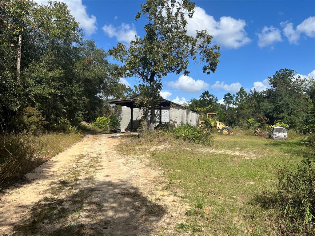 A dirt driveway leads to a concrete block structure with a metal roof and heavy equipment — 4800 CYPRESS STREET, KEYSTONE HEIGHTS, FL