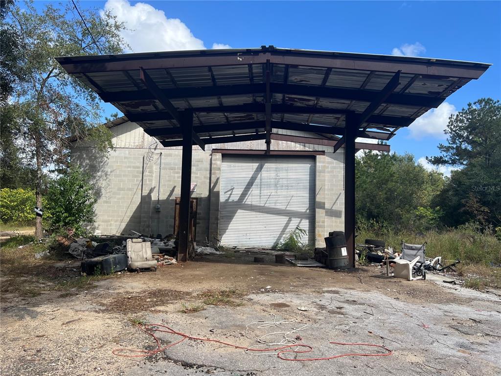 A concrete block warehouse building features a large metal canopy and a roll-up garage door — 4800 CYPRESS STREET, KEYSTONE HEIGHTS, FL