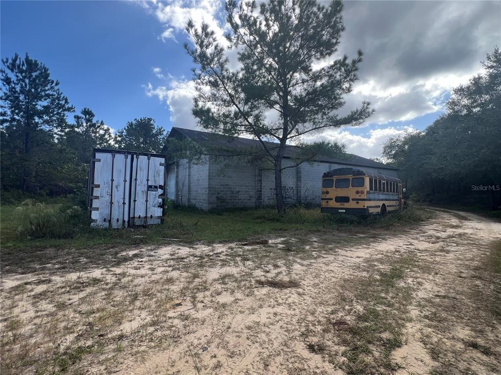 A concrete block building sits on a dirt lot with a shipping container and school bus — 4800 CYPRESS STREET, KEYSTONE HEIGHTS, FL