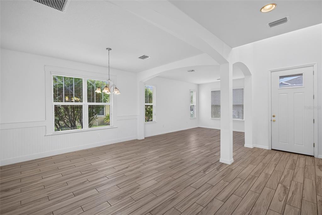 An empty room with white walls, wood-look tile flooring, a dining chandelier, and front door — 5934 ANISE DRIVE, SARASOTA, FL