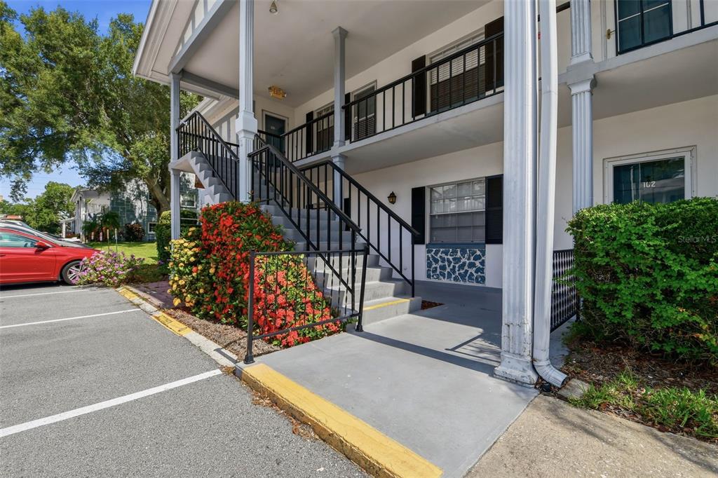 An exterior view of a two-story apartment building with a concrete staircase and parking area — 100 GLENNES LANE UNIT 204, DUNEDIN, FL
