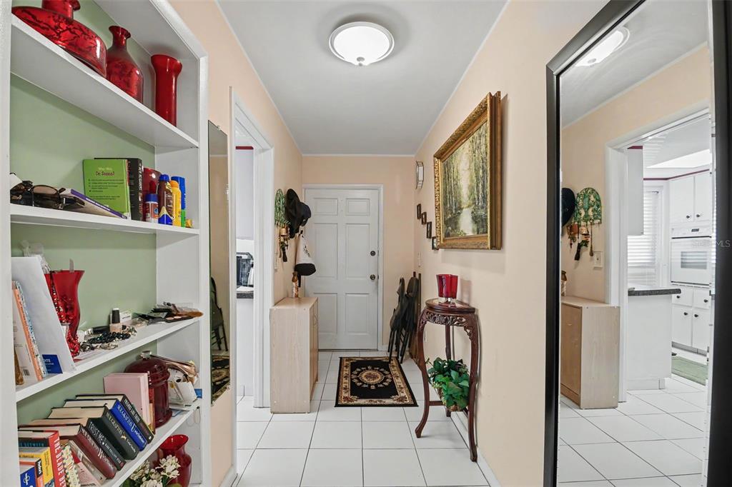 A bright entryway features white tiled floors, a bookshelf, a front door, and a large mirror — 100 GLENNES LANE UNIT 204, DUNEDIN, FL