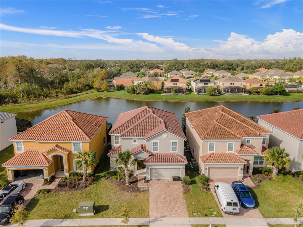 An aerial view shows three suburban houses with tiled roofs situated along a small lake — 2580 SHANTI DRIVE, KISSIMMEE, FL