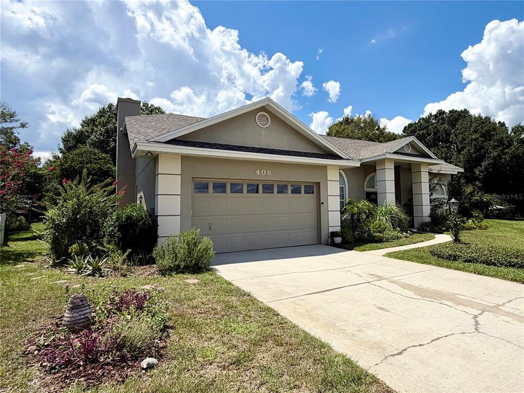 A single-story house with a beige stucco exterior, a two-car garage, and a concrete driveway — 405 VALLEY COURT, WINTER HAVEN, FL