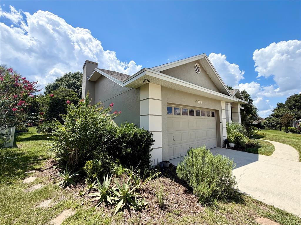 A tan single-story house features a two-car garage, a chimney, and landscaped front yard — 405 VALLEY COURT, WINTER HAVEN, FL