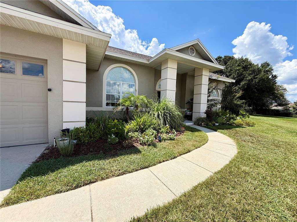 A beige house exterior features a garage, a curved walkway, and a landscaped front yard — 405 VALLEY COURT, WINTER HAVEN, FL