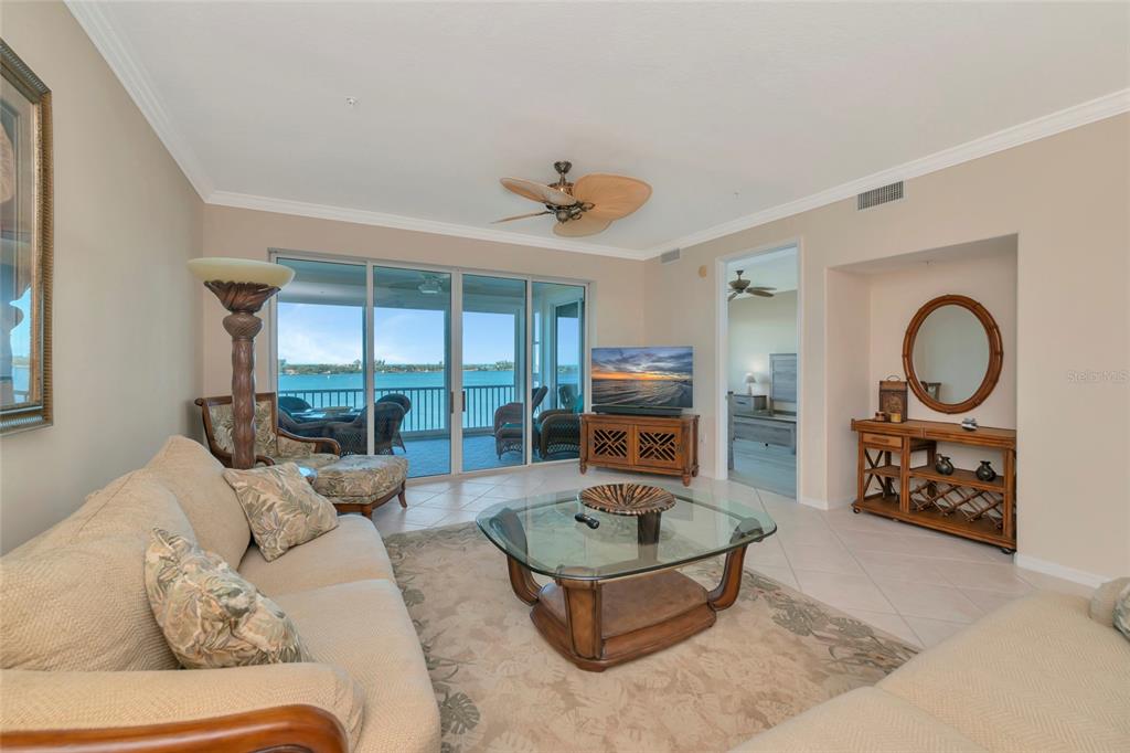 A living room features a glass coffee table, beige sofas, and a view of water — 242 HIDDEN BAY DRIVE UNIT 602, OSPREY, FL