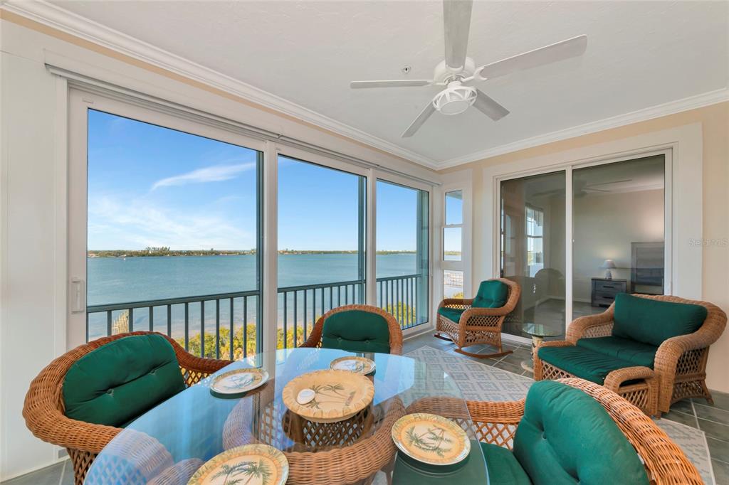 A sunroom with wicker furniture, a glass-topped table, and large windows overlooking the water — 242 HIDDEN BAY DRIVE UNIT 602, OSPREY, FL