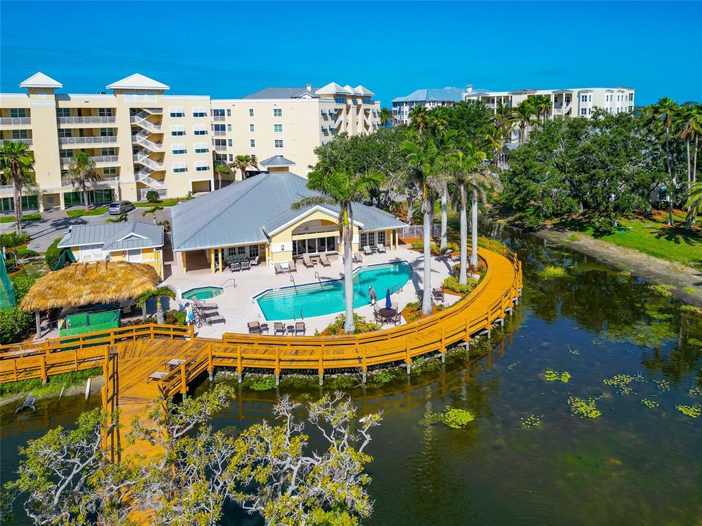 An aerial view shows a swimming pool and wooden deck beside a pond and buildings — 242 HIDDEN BAY DRIVE UNIT 602, OSPREY, FL
