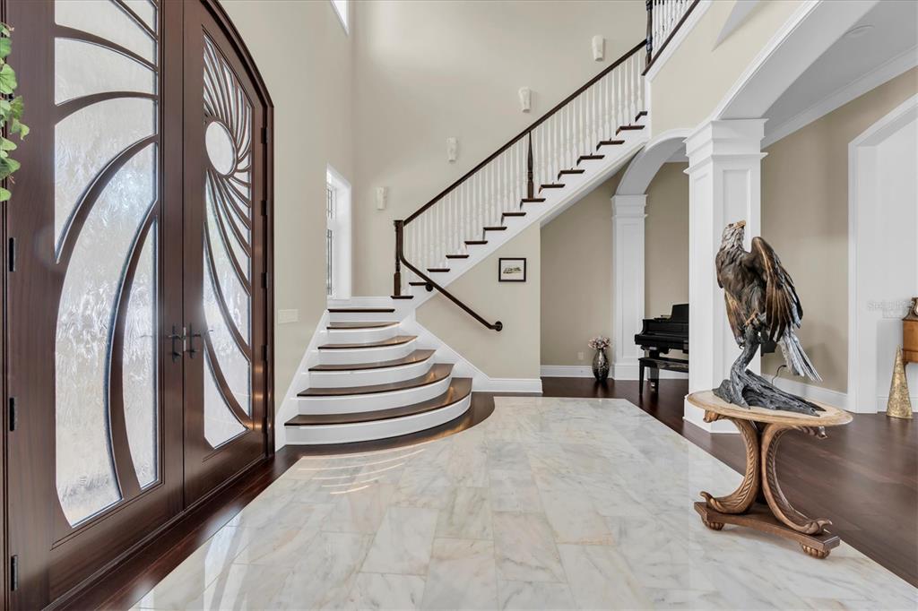 A grand foyer features a curved staircase, marble flooring, and a decorative eagle sculpture — 4650 RIDGE VIEW ROAD, PALM HARBOR, FL