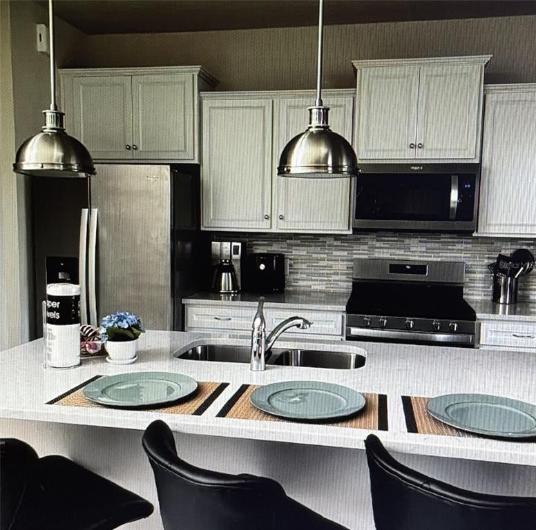 A kitchen features white cabinets, stainless steel appliances, a quartz island, and two pendant lights — 7239 OAKMOSS LOOP, DAVENPORT, FL